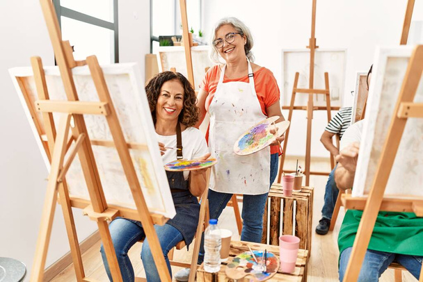 Μια ομάδα μαθητών μέσης ηλικίας ζωγραφίζει στο καλλιτεχνικό στούντιο. Δάσκαλος και μαθήτρια χαμογελά χαρούμενος κοιτάζοντας προς την κάμερα. - Φωτογραφία, εικόνα