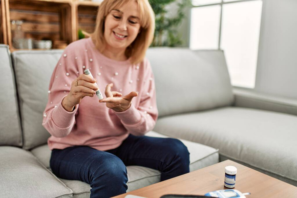 Middelbare leeftijd diabetische vrouw meten glucose met behulp van glucometer thuis. - Foto, afbeelding