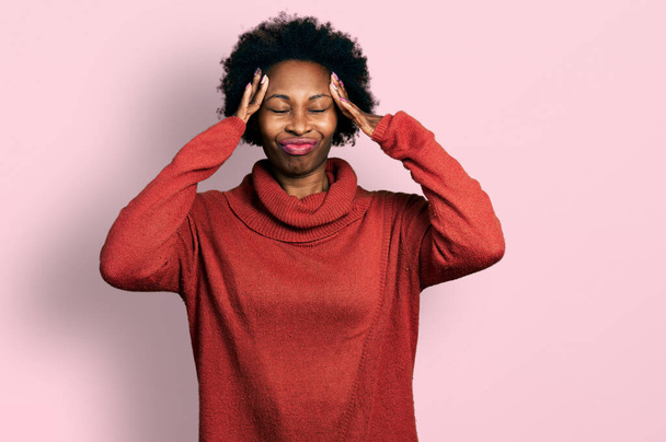 Mujer afroamericana con cabello afro que usa suéter de cuello alto que sufre de dolor de cabeza desesperado y estresado porque el dolor y la migraña. manos en la cabeza.  - Foto, Imagen
