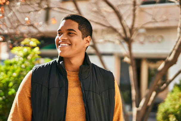 Mladý latinský muž se šťastně usmívá, když stojí ve městě - Fotografie, Obrázek