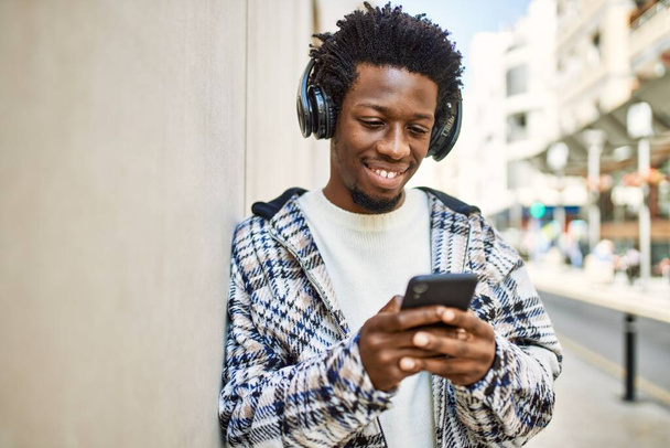 Knappe zwarte man met afro haar dragen van een koptelefoon en het luisteren naar muziek met behulp van smartphone - Foto, afbeelding