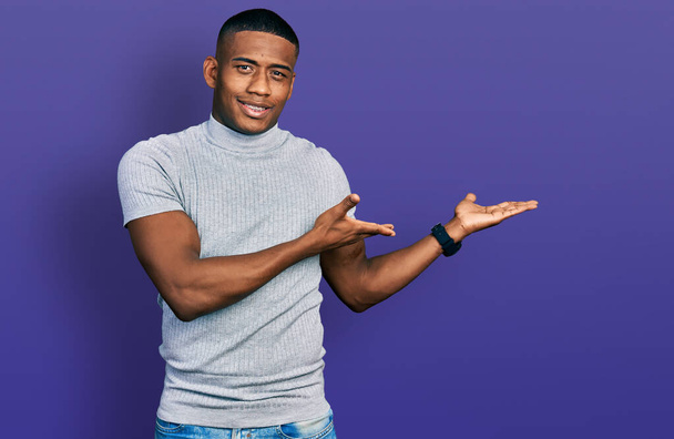 Young black man wearing casual t shirt inviting to enter smiling natural with open hand  - Photo, Image