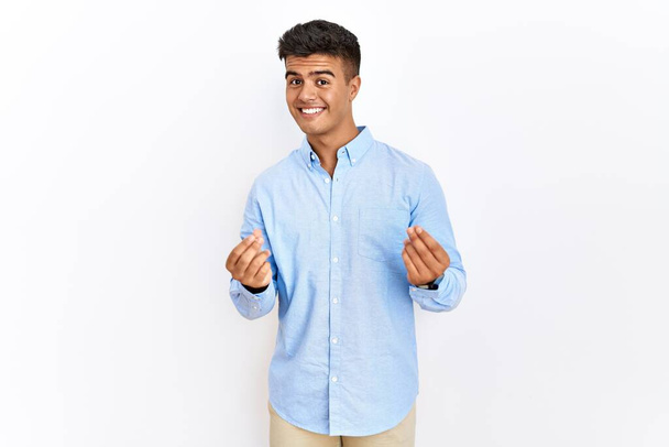 Mladý hispánec v obchodní košili stojící nad izolovaným pozadím, dělá gesto peněz rukama, žádá o výplatu mzdy, milionář podnikání  - Fotografie, Obrázek