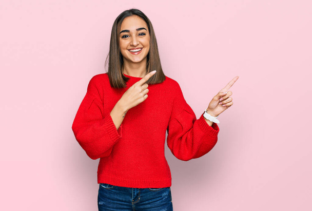 Beautiful brunette woman wearing casual winter sweater smiling and looking at the camera pointing with two hands and fingers to the side.  - Photo, Image