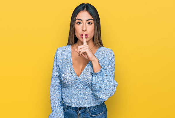 Junge hispanische Frau in lässiger Kleidung, die mit dem Finger auf den Lippen um Ruhe bittet. Schweigen und geheimes Konzept.  - Foto, Bild