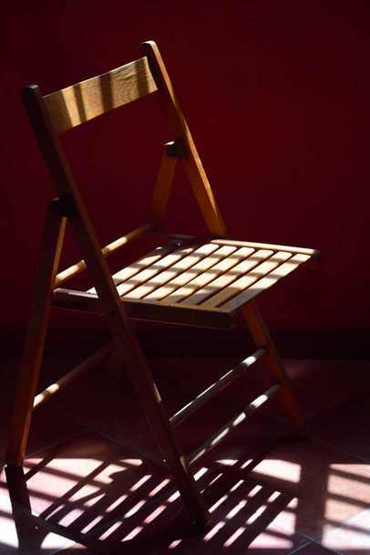 A wooden chair stands in front of a red wall and the shadow of the chair falls on the floor, in a room in portrait format - Photo, Image