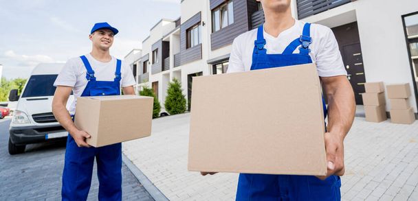 Two removal company workers unloading boxes from minibus into customers home - 写真・画像