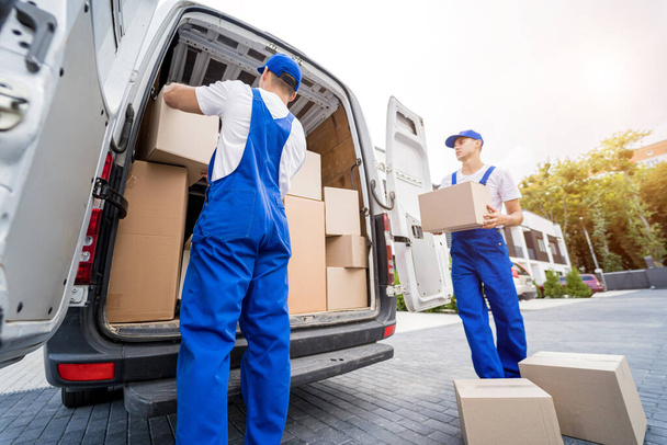 Two removal company workers are loading boxes and furniture into a minibus. - 写真・画像