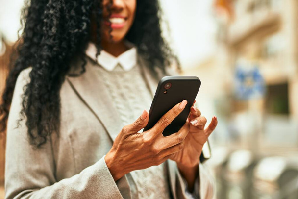 Middelbare leeftijd Afrikaanse Amerikaanse zakenvrouw met behulp van smartphone in de stad. - Foto, afbeelding