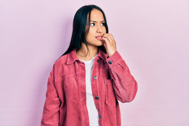Schöne hispanische Frau mit Nasenpiercing in lässiger pinkfarbener Jacke, die gestresst und nervös aussieht, die Hände auf den Mund beißenden Nägeln. Angstproblem.  - Foto, Bild