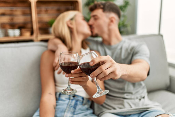 Young caucasian couple kissing and toasting with red wine at home. - Foto, immagini
