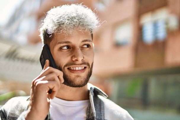 Молодий іспаномовний чоловік посміхається щасливий розмовляючий смартфон у місті
. - Фото, зображення
