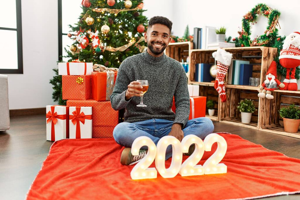 Jeune homme afro-américain souriant heureux de célébrer 2022 nouvelle année boire du champagne à la maison. - Photo, image