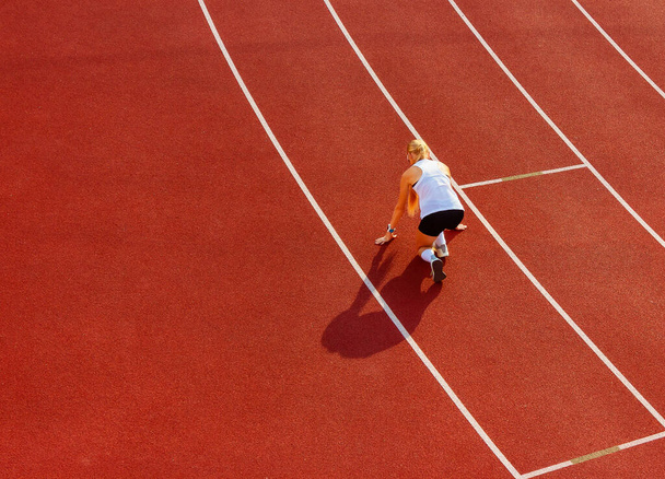 νεαρή γυναίκα με αθλητική στολή σκύβει για ένα χαμηλό ξεκίνημα στο στάδιο που τρέχει, πίσω όψη. αθλητική εκπαίδευση και άσκηση. υγιεινός τρόπος ζωής - Φωτογραφία, εικόνα