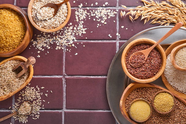 White, brown and red rice, buckwheat, millet, corn groats, quinoa and bulgur in wooden bowls on a brown stone kitchen table. Gluten-free cereals. Top view with copyspace - Foto, Imagem