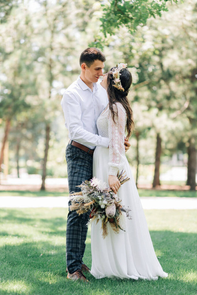 Beautiful wedding couple, Handsome groom and bride in white wedding dress, newlyweds laugh and kiss, in the park, Concept of love and happiness, wedding day, wedding ceremony in boho style - Фото, зображення