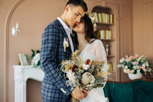 Happy bride and groom holding a bouquet of wedding flowers, Happy young couple, Happy wedding day, Bride and groom posing and looking at each other in the studio - Foto, Imagen