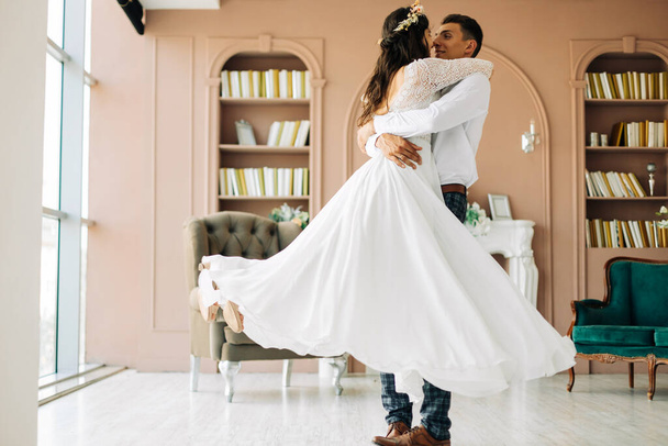 Happy wedding couple, attractive bride and groom hug each other, the groom hugs and holds the bride in his arms and circles her, Happy wedding day, the bride and groom in the studio - Fotó, kép
