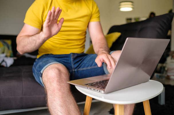 Freelancer tiene una reunión virtual, Hombre hablando en línea con los empleados a través de la conexión de vídeo utilizando el ordenador portátil en la mesa de café en la sala de estar - Foto, imagen