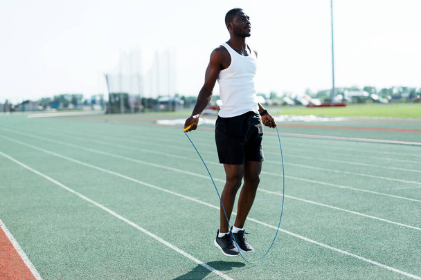 An African-American male track and field athlete in a white T-shirt trains before a jump rope race - Фото, изображение