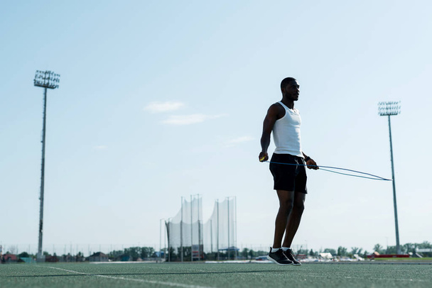 A purposeful African-American male track and field athlete in a white T-shirt jumps on a rope - Foto, Imagem