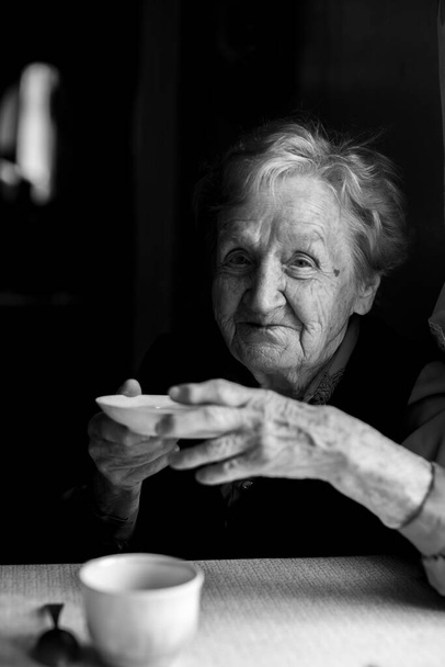 Old granny is drinking tea. Black and white portrait. - Photo, Image