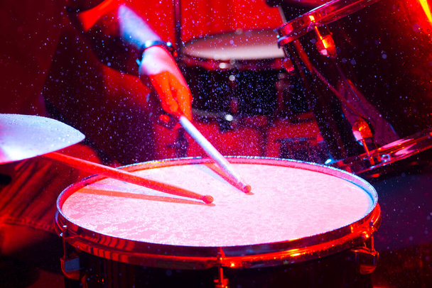 man playing the snare drum on a beautiful colored background, the concept of musical instruments with splashing water on dark background with red studio lighting. Dynamic scene. - Photo, Image