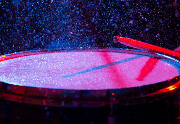 Bastoncini di tamburo colpiscono rullante tamburo con spruzzi d'acqua su sfondo scuro con illuminazione studio rosso e blu. Scena dinamica - Foto, immagini
