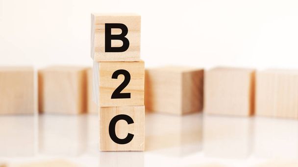 文字B2Cと木製のキューブ垂直ピラミッド、白の背景に配置し、テーブルの表面からの反射、ビジネスコンセプト。b2c -消費者向けビジネスの略. - 写真・画像