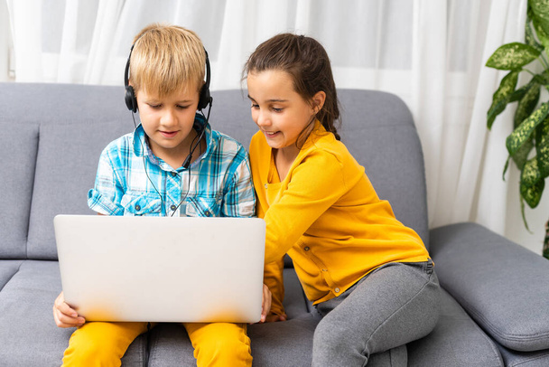 Технологии, bkids дружба и коммуникация концепция - два милых подростка с помощью планшета и ноутбука, сидя на диване в гостиной на дому - Фото, изображение