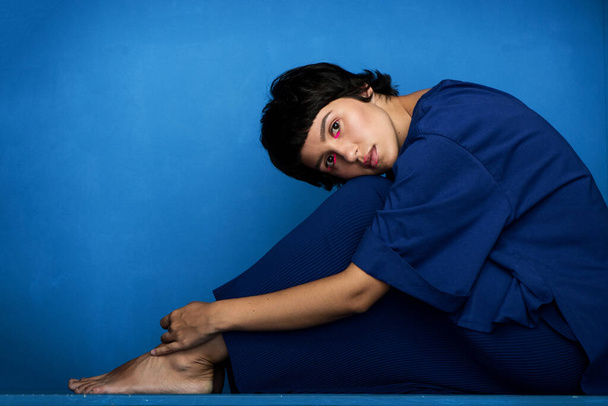 Young beautiful woman sitting on blue background. - Fotoğraf, Görsel