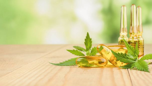 cannabidiol capsules and ampoules and fresh cannabis leaves on a wooden table - Photo, Image