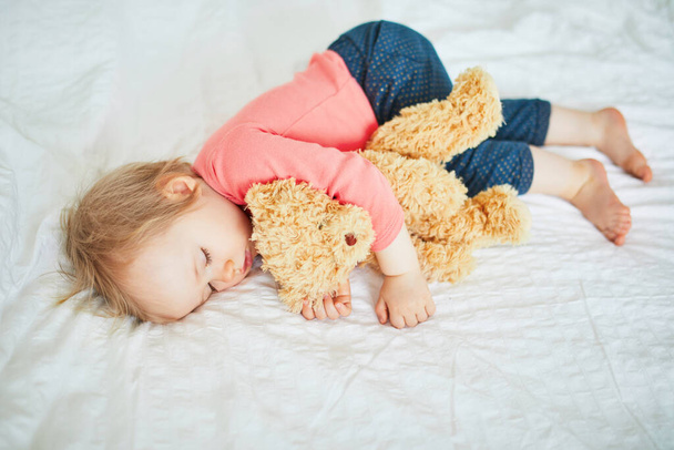 Adorable baby girl sleeping with her favorite toy. Little child having a day nap and hugging a teddy bear. Infant kid resting in nursery - Foto, afbeelding
