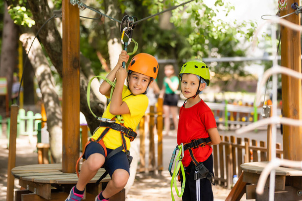Child in forest adventure park. Kids climb on high rope trail. Agility and climbing outdoor amusement center for children. Little girl playing outdoors. School yard playground with rope way. - Foto, imagen