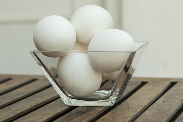 eieren in een transparante glazen kom isoated op houten tafel. - Foto, afbeelding