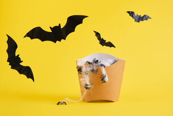fast food packaging for fries with cobwebs and spiders, decorative bats, halloween concept, yellow background halloween decoration concept - Foto, Bild