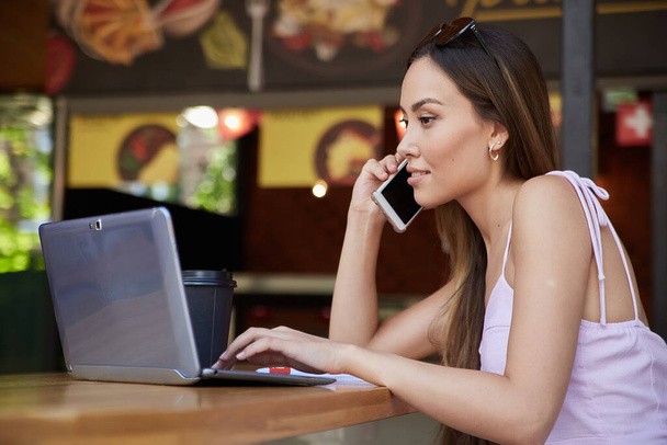 atractiva hembra en vestido con taza de café trabajando en la cafetería, llamando por teléfono - Foto, imagen
