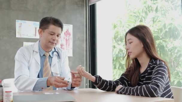 Férfi orvos megvizsgálja a vért egy ázsiai felnőtt nő inzulinmérő készülék cukorbetegség és egészségügyi vizsgálatok a kórházi klinikán. Laboratóriumi elemzés glükózkontroll és orvosi kezelés céljából. - Felvétel, videó
