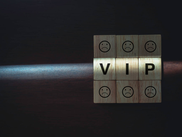 VIP words and boring faces emoticon on wooden blocks with the light on dark wood background with copy space. Privileges infringing on other people freedoms and civil liberties concept. - Photo, Image