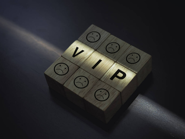 VIP words and boring faces emoticon on wooden blocks with the light on dark wood background, close up. Privileges infringing on other people freedoms and civil liberties concept. - Photo, Image