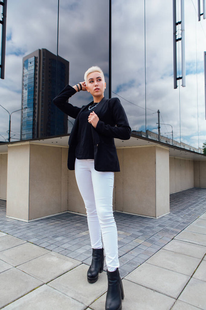 Young stylish business woman with short hair and nose piercing. Confident girl look like lesbian standing near business center with mirror walls - Φωτογραφία, εικόνα