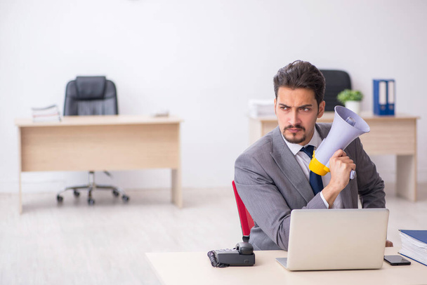 Joven empleado masculino sosteniendo megáfono en el lugar de trabajo - Foto, Imagen