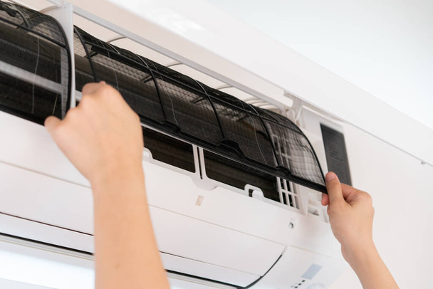Asian woman changing a dirty and dusty air conditioner filter in bedroom. Woman removing a dirty air filter inside air conditioner. - Foto, Bild