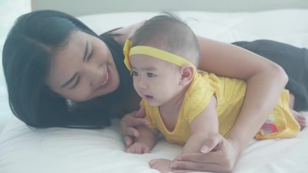 Молода азіатська мати цілує щоку маленької дівчинки з телятиною на ліжку в спальні, мама любить новонароджених і догляд, мати з виразом з дитиною разом, мати і дочка, концепція сім'ї
. - Кадри, відео