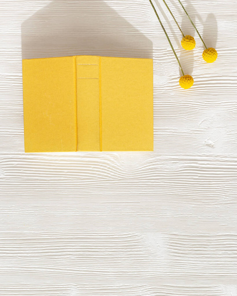 Close-up of open book in yellow cover on white wooden table. Concept of reading books and taking  break from gadgets.  - Fotografie, Obrázek