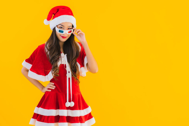 Portrét krásná mladá asijská žena nosit vánoční oblečení klobouk s popcornem a 3D brýle připravené sledovat film na žlutém izolovaném pozadí - Fotografie, Obrázek