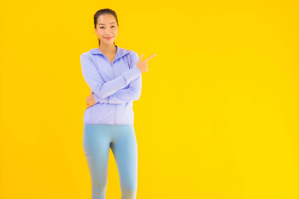 Porträt schöne junge asiatische Sportlerin mit Sportbekleidung bereit für die Übung auf gelbem isolierten Hintergrund - Foto, Bild