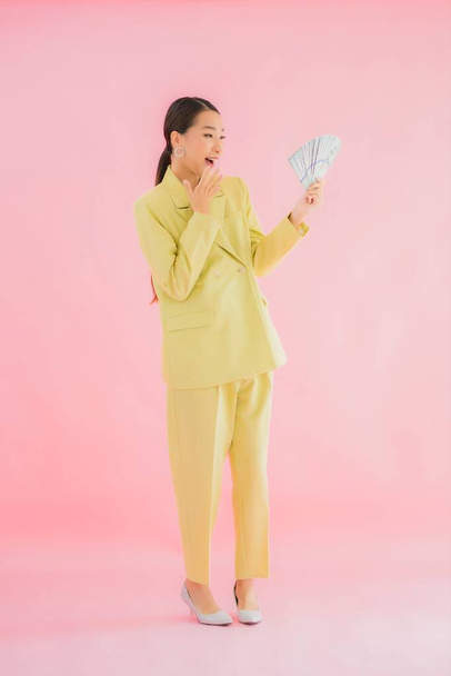 Porträt schöne junge asiatische Geschäftsfrau mit viel Bargeld oder Geld auf farbigem Hintergrund - Foto, Bild