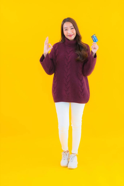 Retrato hermosa joven asiática mujer con tarjeta de crédito para compras en línea en amarillo aislado fondo - Foto, imagen