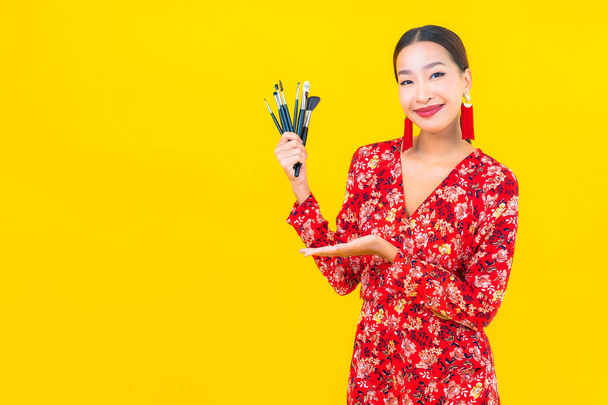 Muotokuva kaunis nuori aasialainen nainen meikki harja ja kosmeettinen keltaisella pohjalla - Valokuva, kuva